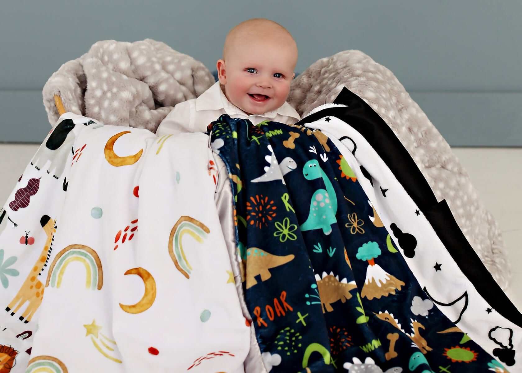 Baby boy sitting in a basket overflowing with various baby boy patterned blankets. 
