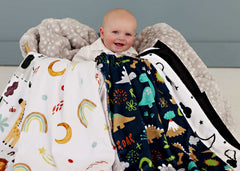 Baby boy sitting in a basket overflowing with various baby boy patterned blankets. 