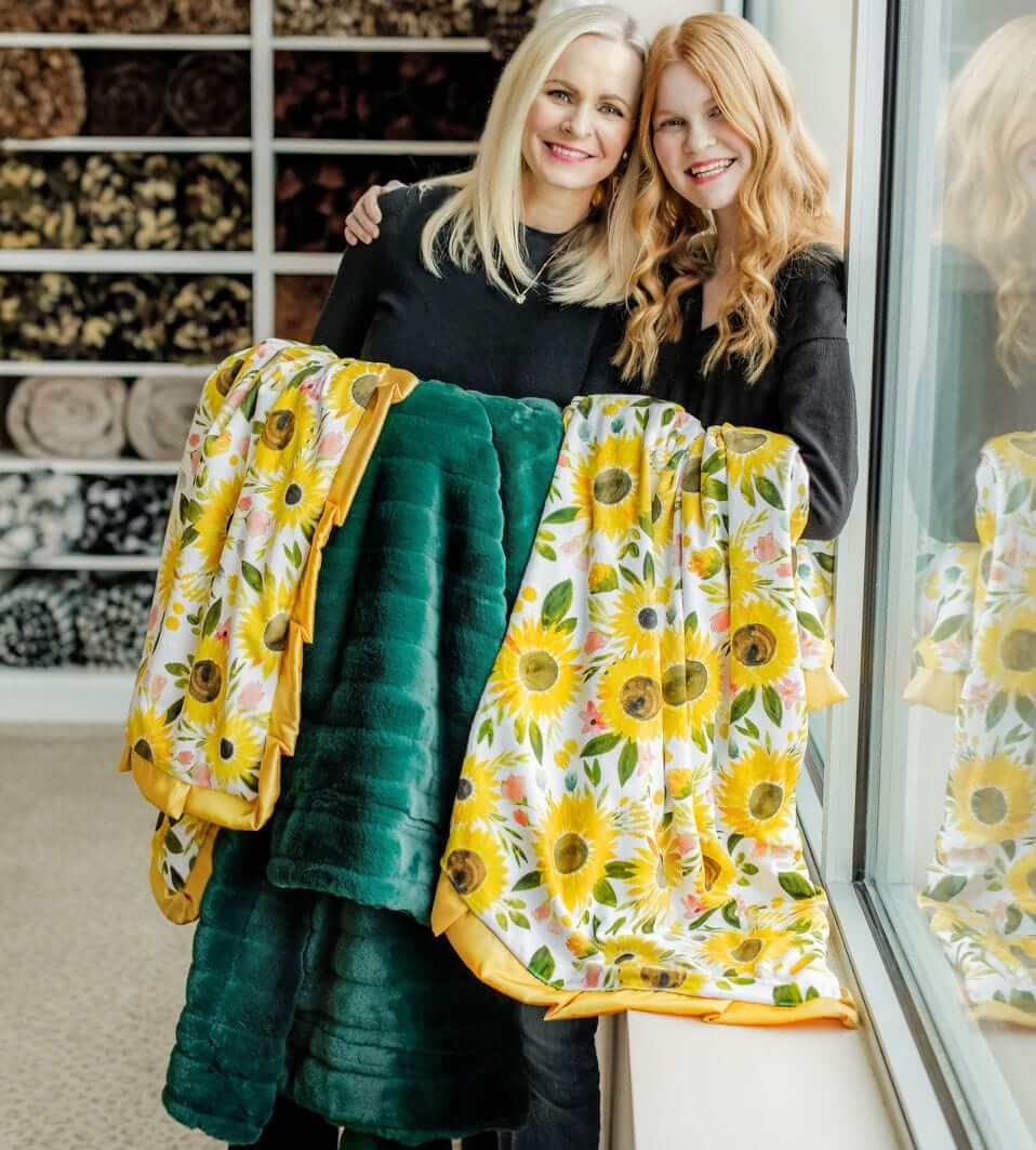 Mother and daughter holding water colored sunflower Little Miss Sunshine Blanket and emerald minky blankets.