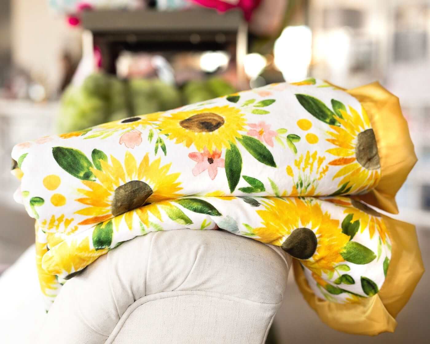 Yellow watercolor sunflower Little Miss Sunshine Blanket folded and laid on the back of a cream chair.