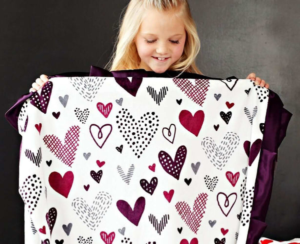 Little girl holding up Love Note Plum blanket from Minky Couture.