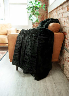 Lush Black Onyx Blanket draped over a brown leather chair, showcasing its softness and luxurious texture.