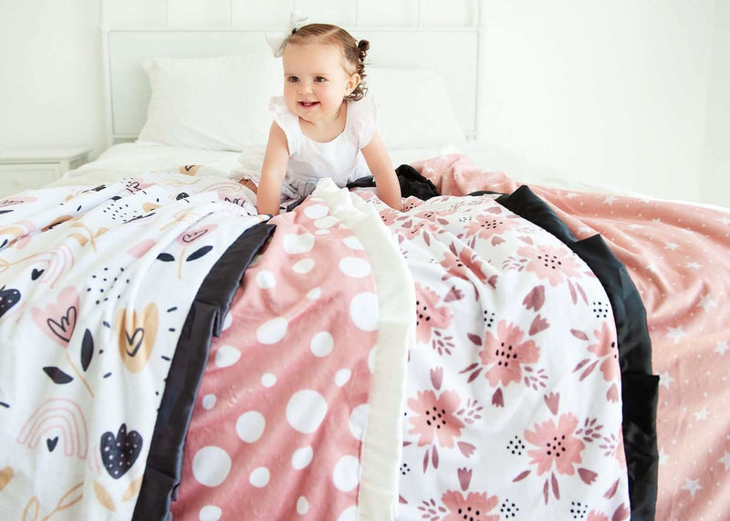 Toddler girl crawling on four blush pink floral, polka dot and star blankets by Minky Couture. 