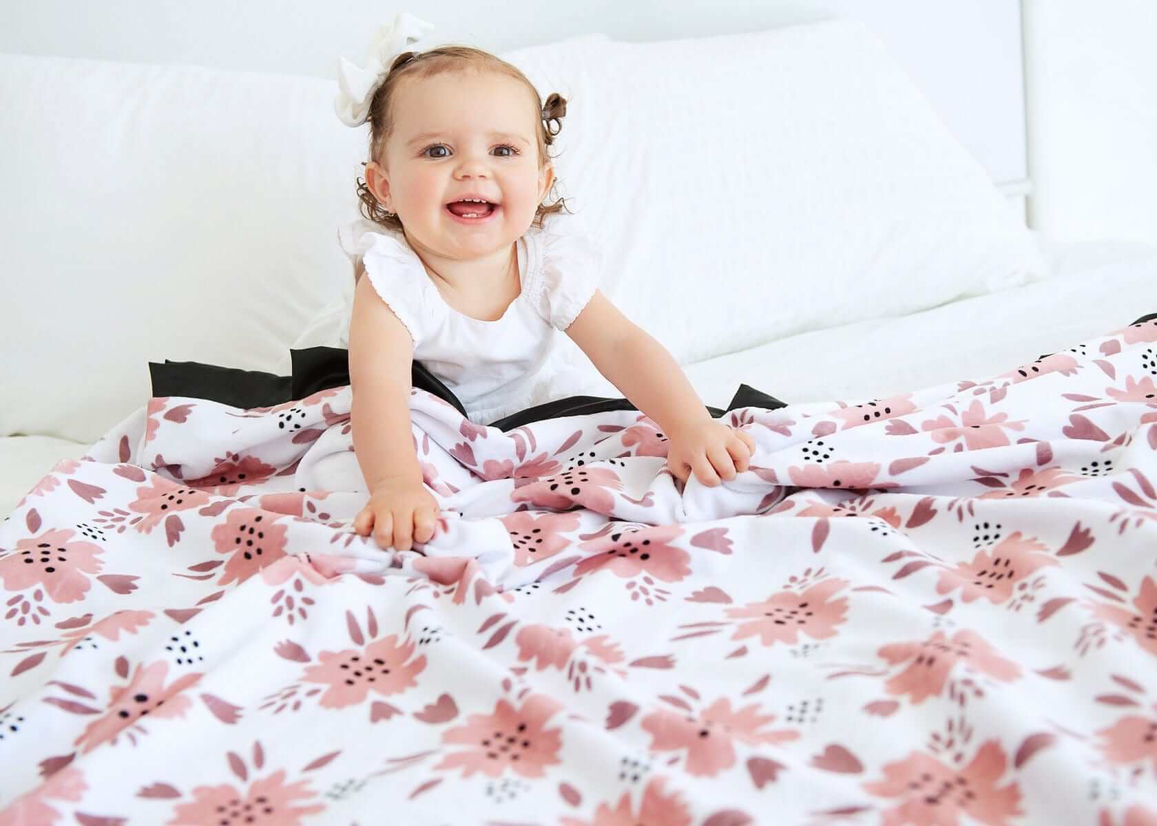 Toddler girl sitting under a pink Apricot Blossom themed blanket. 