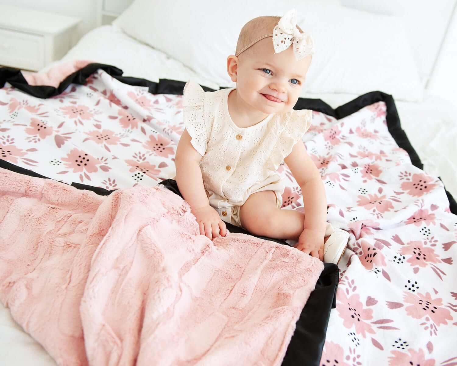 Baby sitting on the Apricot Blossom Blanket featuring blush and mauve floral patterns with plush backing.