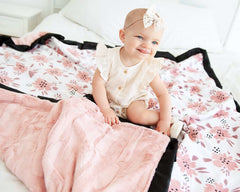 Baby sitting on the Apricot Blossom Blanket featuring blush and mauve floral patterns with plush backing.