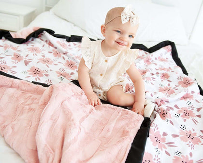 Baby sitting on the Apricot Blossom Blanket featuring blush and mauve floral patterns with plush backing.