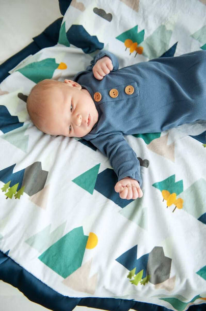 Baby lounging on the cozy Mountain Tops Blanket with geometric mountain designs.