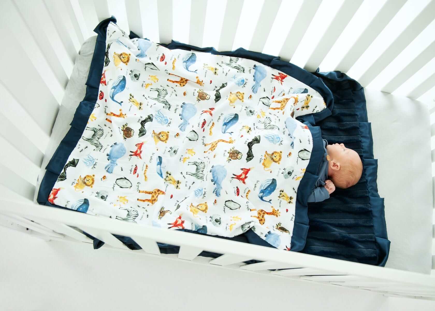 ABC Zoo Blanket in crib with baby, colorful animal pattern, navy plush backing, vibrant decor for nursery.
