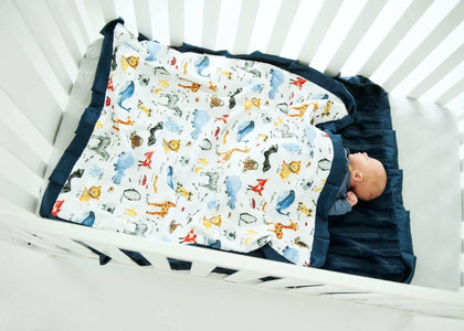ABC Zoo Blanket in crib with baby, colorful animal pattern, navy plush backing, vibrant decor for nursery.