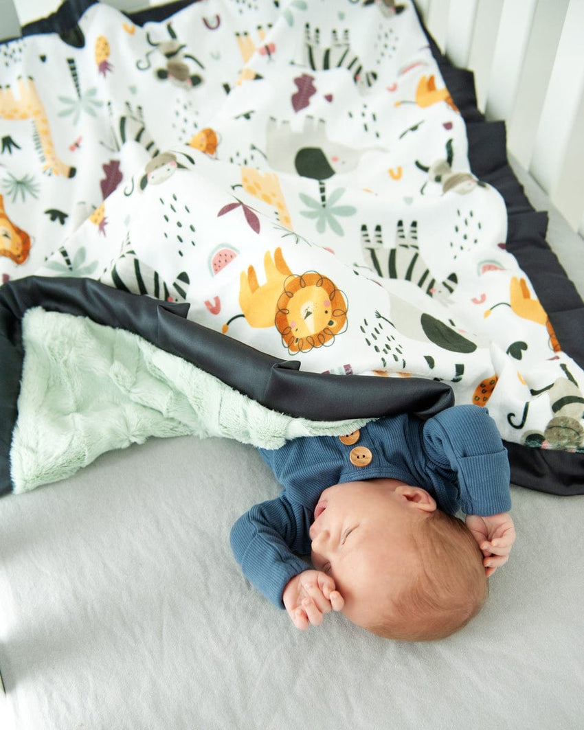 Baby boy laying in a crib with a cartoon zoo animal themed blanket.