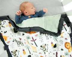 Baby snuggled with Zoo Day Blanket featuring colorful zoo animals like lions and monkeys.