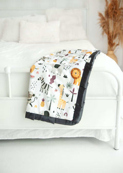 Zoo Day Blanket draped over a bed, featuring playful prints of lions, zebras, and monkeys.