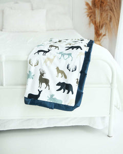 Cozy Teton Mist Blanket featuring woodland animals in navy and light blue on an off-white background.