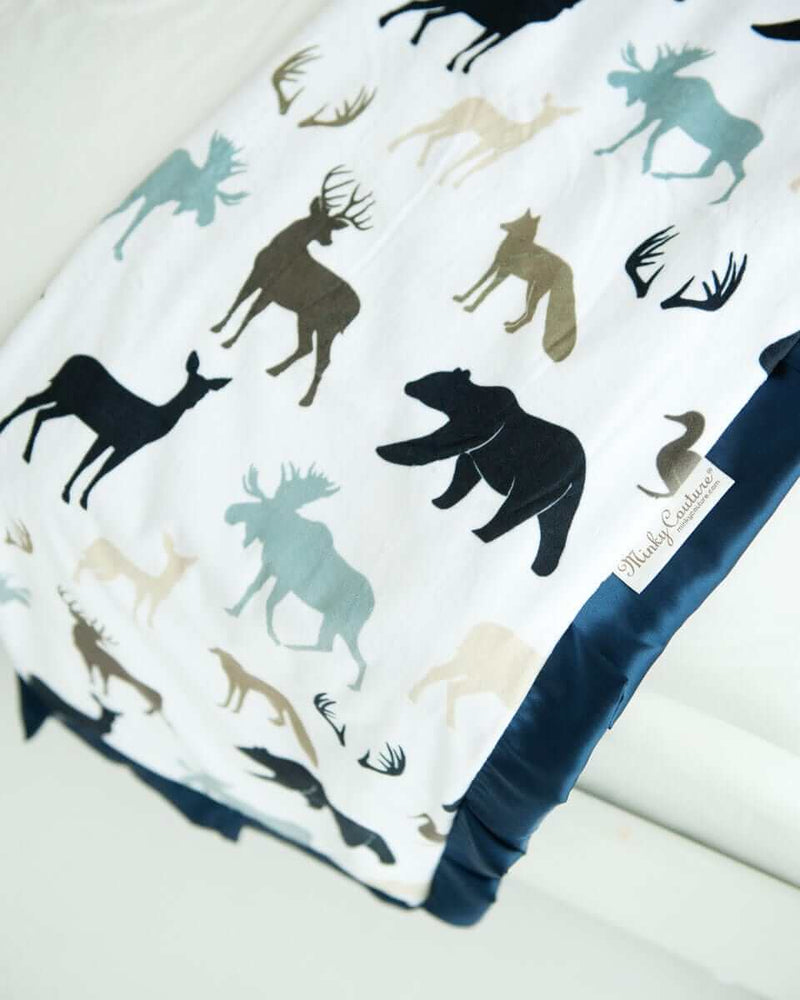 Teton woodland animal blanket by minky couture folded and hanging over the end of a bed.