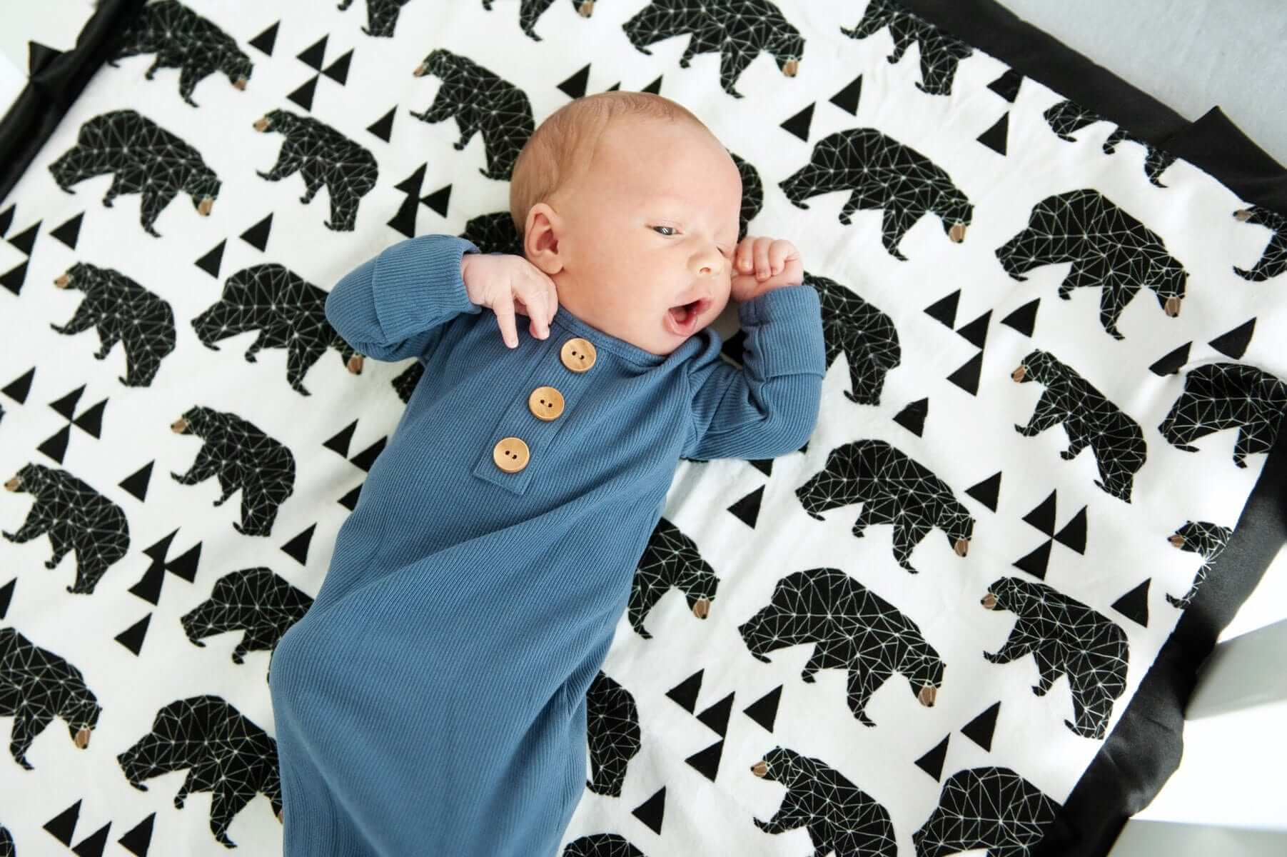 Newborn baby laying on top of a bear patterned blanket. 
