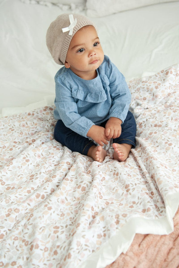 Baby girl sitting on top of a floral blanket with small flowers and greenery on it in shades of blush.
