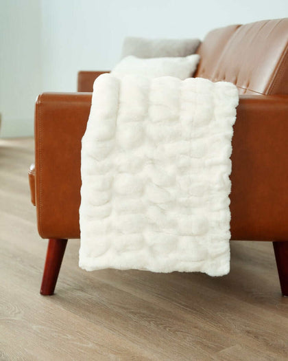 White Glove Hugs Cream Minky Couture blanket draped over a brown leather couch, showcasing its soft texture and cozy design.