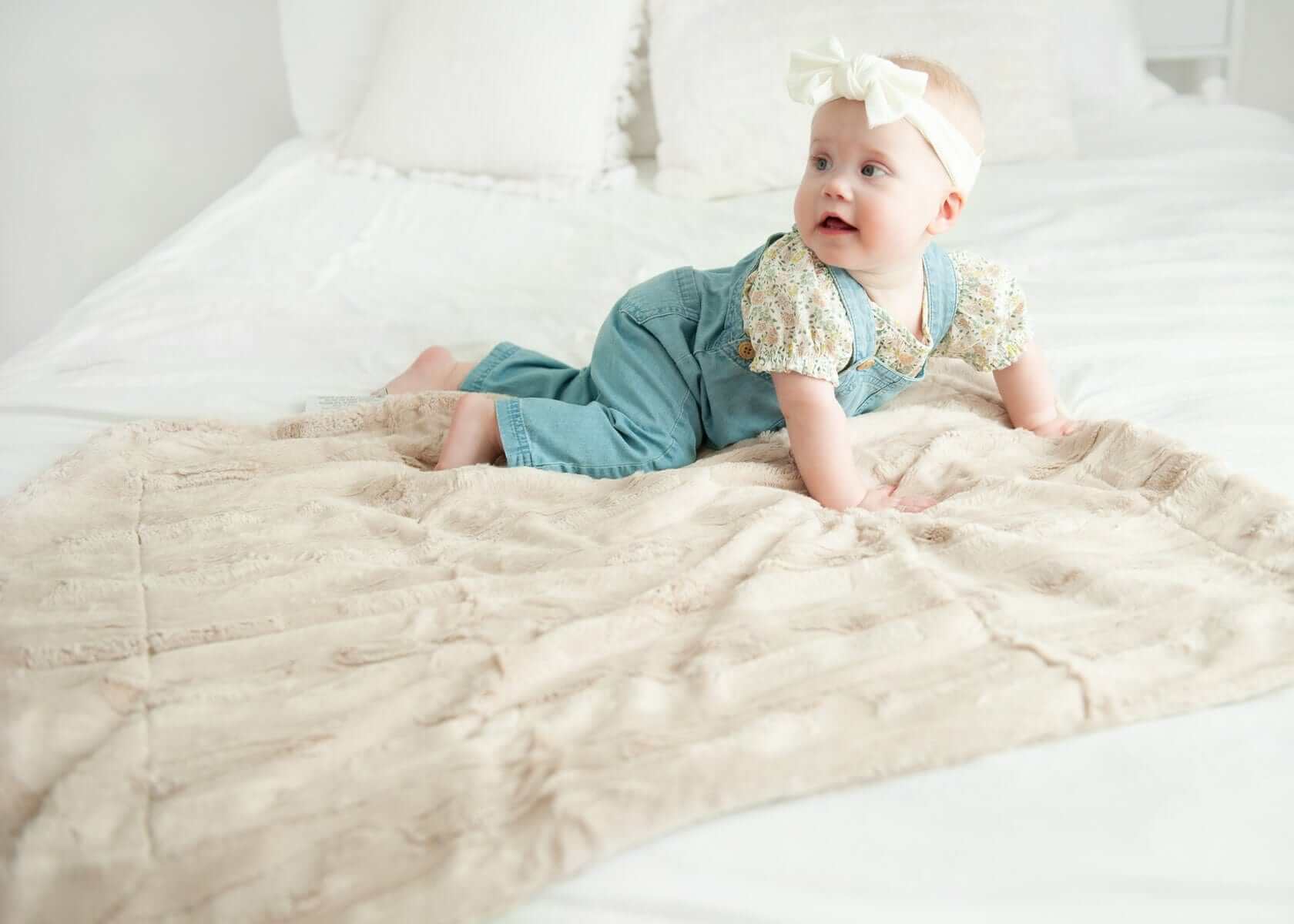 Baby enjoying the cozy Sorbet Almond Croissant Blanket on a white bed.