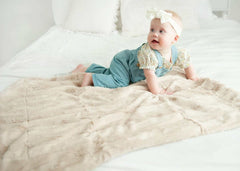 Baby enjoying the cozy Sorbet Almond Croissant Blanket on a white bed.