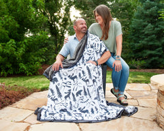 Wilderness Blanket featuring outdoor wildlife design, cozy charcoal minky backing, and two people enjoying it outdoors.