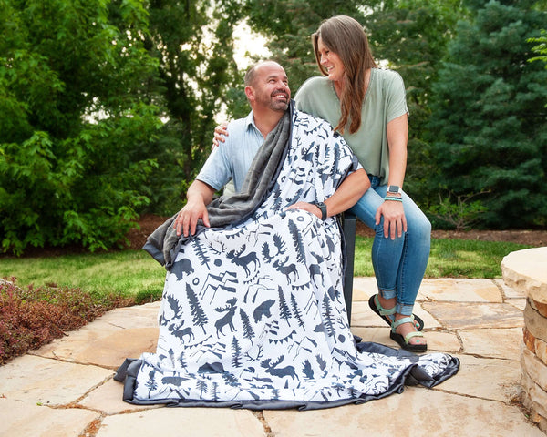 Wilderness Blanket featuring outdoor wildlife design, cozy charcoal minky backing, and two people enjoying it outdoors.