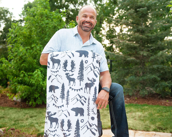 Wilderness Blanket featuring outdoor wildlife patterns with moose and bears held by a smiling man outdoors.