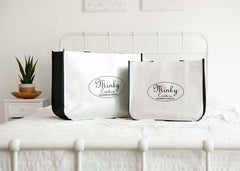 Two Minky Couture reusable Shopping Bags displayed on a bed, showcasing their design and versatility for various uses.
