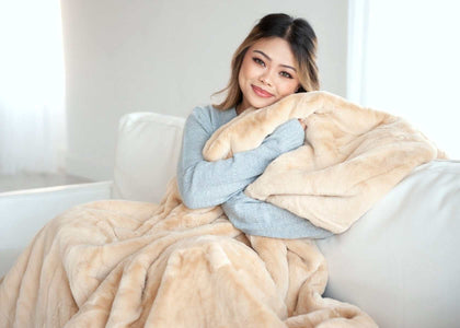 A cozy scene featuring a woman wrapped in a Lush True Caramel Blanket, enjoying warmth on a sofa.