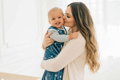 Mother kissing baby wearing Navy Stars and Moons Wearable Minky Blanket, highlighting comfort and safety.
