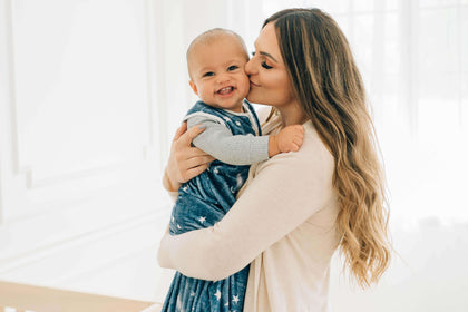 Mother kissing baby wearing Navy Stars and Moons Wearable Minky Blanket, highlighting comfort and safety.