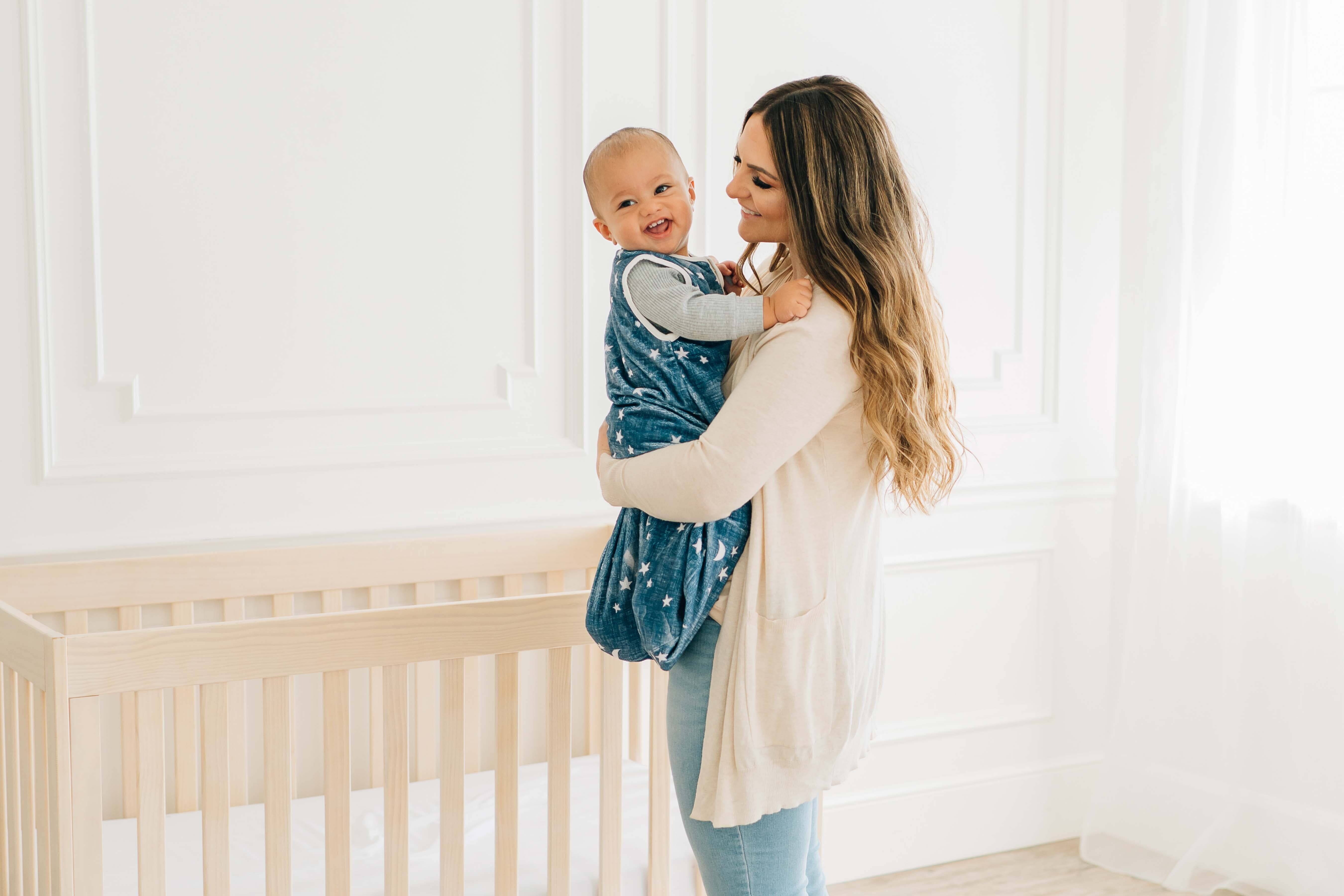 Navy Stars and Moons Wearable Minky Blanket being held by a mother in a nursery setting with a crib.