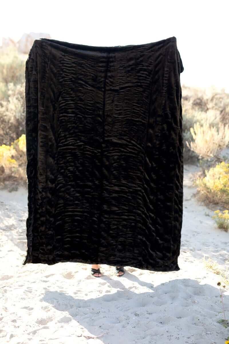 Ruched black stretchy Minky Couture blanket held high to show entire blanket texture. 