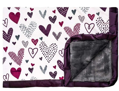 Love Notes Plum Minky Couture designer blanket laying flat with edge turned up. Doodled purple hearts with charcoal faux fur back and plum satin ruffle. 