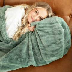 Young woman laying on a brown leather couch hugging a thick mist green plush blanket.