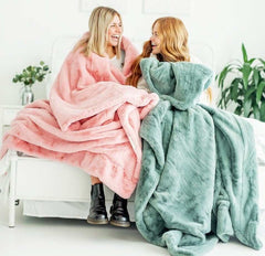 Two women wrapped in soft blankets, one in a Lush Pretty Pink Blanket, enjoying cozy moments together.
