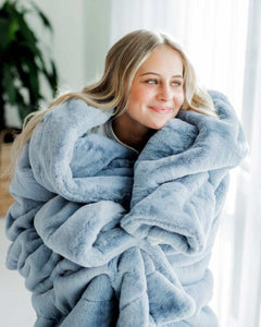 Cozy woman wrapped in a Lush Denim Blanket, showcasing its thick plush texture and stunning denim blue hue.